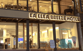 Die Fassade des La Ella Breeze Hotels zeigt eine einladende Atmosphäre mit warmem Licht und modernen Möbeln im Innenbereich.