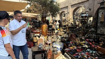 Ein Mann erklärt einem Jungen die verschiedenen Antiquitäten auf einem lebhaften Markt in Dubai, umgeben von vielen Objekten.