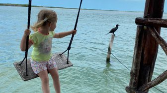 Kind schaukelt über dem smaragdgrünen Wasser mit Blick auf die Lagune – Mexiko Familienreise