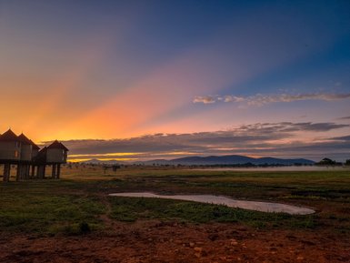 Die Silhouette von erhöhten Lodges vor einem atemberaubenden Sonnenaufgang über der weiten Savanne.