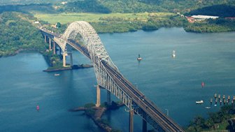 Eine beeindruckende Brücke überspannt das Wasser des Panamakanals, umgeben von grün bewaldeten Hügeln und klarem Himmel.