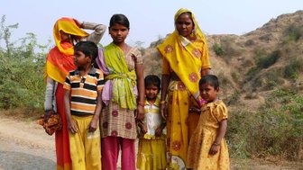 Eine indische Familie steht auf einer Straße, umgeben von sanften Hügeln, in bunten traditionellen Kleidern.