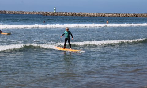 Ein junger Surfer balanciert auf einem orangefarbenen Brett und reitet eine Welle im klaren Wasser des Strandes.