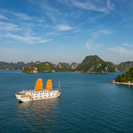 Ein traditionelles Boot mit orangefarbenen Segeln gleitet ruhig durch das klare Wasser der Halong-Bucht, umgeben von grünen Inseln.