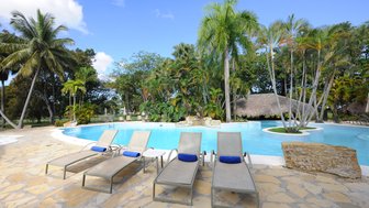 Vier Liegen stehen am Pool mit Palmen im Hintergrund