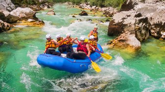 Eine Gruppe von sechs Personen paddelt in einem blauen Raft durch einen klaren, grünen Fluss, umgeben von Felsen und Bäumen.