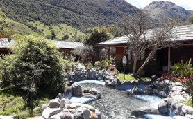 Eine malerische Landschaft mit einem klaren Wasserlauf, umgeben von üppigem Grün und rustikalen Holzhütten.