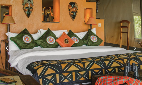 Ein stilvolles Zimmer im Kilima Camp mit bunten Kissen und afrikanischen Masken an der Wand, das eine gemütliche Atmosphäre schafft.