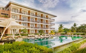 Ein modernes Resort mit mehreren Etagen, das von üppigem Grün und einem klaren Pool umgeben ist, unter einem strahlend blauen Himmel.