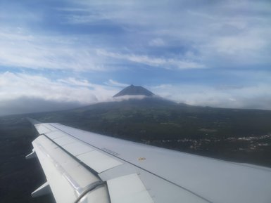 Die Sicht zeigt einen Vulkan, der majestätisch aus einer grünen Landschaft emporragt, während Wolken ihn umgeben.