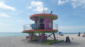 Ein lebhaftes, pinkfarbenes Rettungsschwimmerhaus steht am Strand von Miami, umgeben von feinem Sand und klarem Wasser.