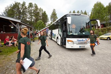 Eine Gruppe junger Menschen verlässt einen Reisebus in einer ländlichen Umgebung, umgeben von Bäumen und Hütten.