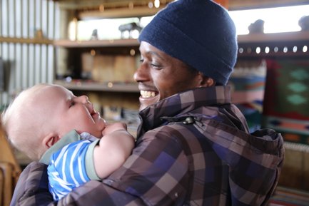 Einheimischer trägt lächelnd ein Baby auf dem Arm – Südafrika Familienreise