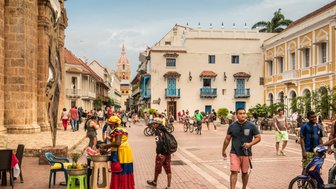 Eine lebhafte Straßenszene in Cartagena, wo Menschen flanieren und ein Verkäufer frisches Obst anbietet.
