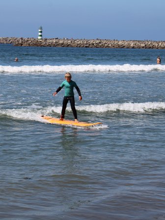 Ein junger Surfer balanciert auf einem orangefarbenen Brett und reitet eine Welle im klaren Wasser des Strandes.