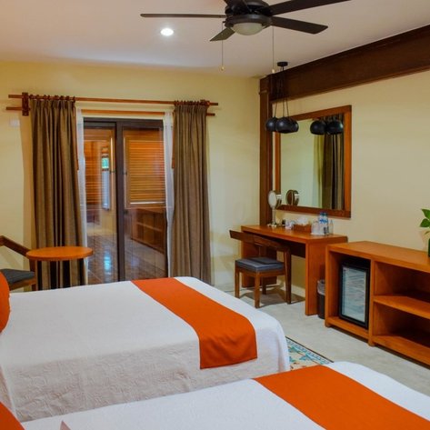 Zwei Einzelbetten mit orangefarbenen Kissen in einem hellen, modernen Hotelzimmer mit Holzdetails.