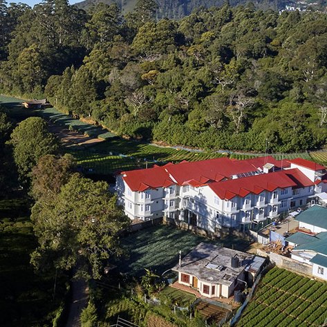 Ein malerisches Hotel mit roten Dächern, umgeben von üppigem Grün und Teeplantagen in Sri Lanka.