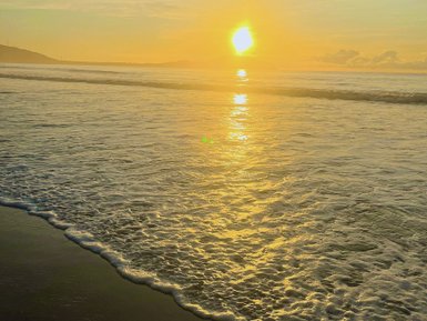 Die Sonne geht über dem ruhigen Meer unter, während sanfte Wellen den Strand umspülen und goldenes Licht reflektieren.