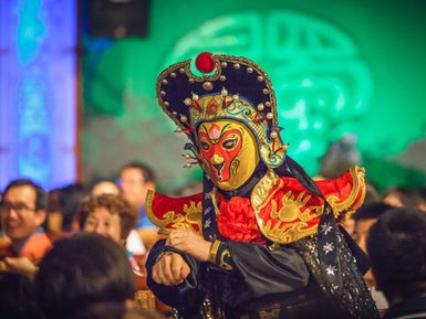 Ein Künstler in traditioneller Sichuan-Oper trägt eine auffällige Maske und ein prächtiges Kostüm, während er das Publikum unterhält.