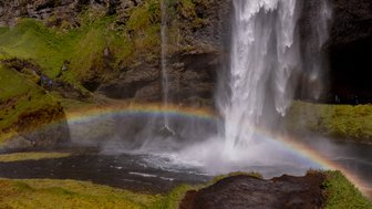 Ein majestätischer Wasserfall stürzt in einen klaren Teich, während ein Regenbogen die Szenerie erhellt.