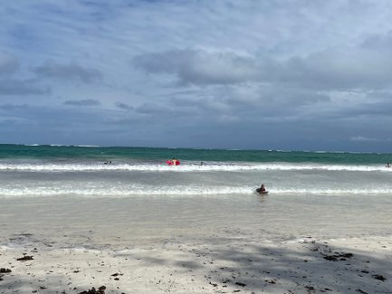 Ein Kind surft auf einer Welle, während andere im Hintergrund im Wasser spielen, umgeben von einem schönen Strand.