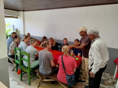 Eine Gruppe von Menschen hört gebannt einem Koch zu, während verschiedene Zutaten auf dem Tisch präsentiert werden.
