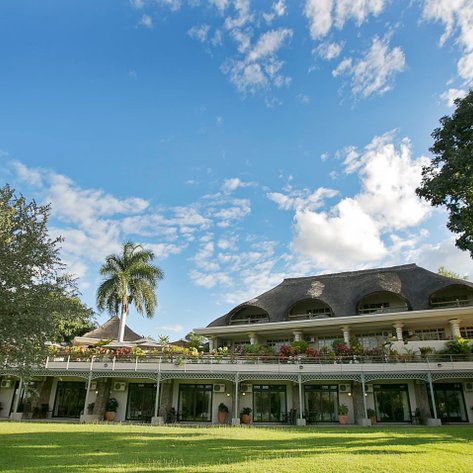 Das Ilala Lodge Hotel in Botswana zeigt eine elegante Fassade mit einem begrünten Garten und strahlend blauem Himmel.
