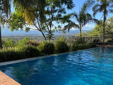 Ein glitzernder Pool umgeben von üppigem Grün und Palmen, mit einem atemberaubenden Blick auf die Landschaft im Hintergrund.