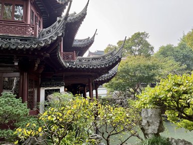 Ein traditionelles chinesisches Gebäude mit geschwungenem Dach, umgeben von üppigem Grün und einem ruhigen Teich.