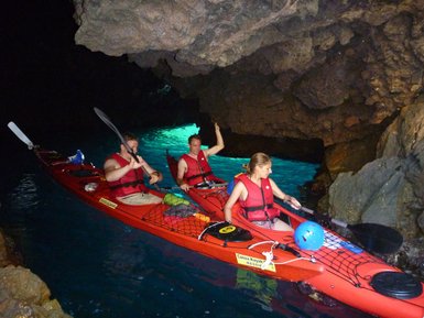 Drei Kajakfahrer paddeln in einer Höhle, umgeben von glitzerndem Wasser und beeindruckenden Felsformationen.
