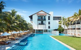 Ein modernes Hotelgebäude mit einem großen Pool, umgeben von Palmen und Liegen, strahlt tropische Entspannung aus.