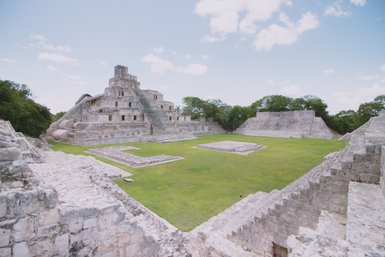 Die beeindruckenden Ruinen einer alten Pyramide stehen majestätisch in einer weitläufigen, grünen Landschaft unter einem blauen Himmel.