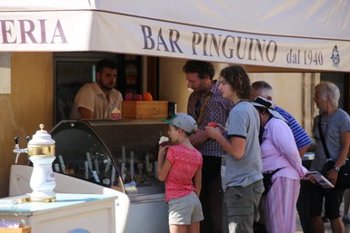 Eine Gruppe von Menschen steht an einem Eisstand, während sie verschiedene Eissorten auswählen und genießen.