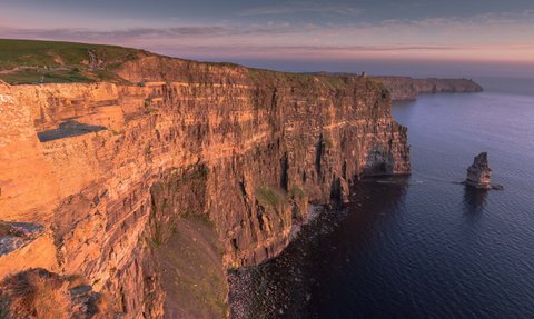 Die beeindruckenden Cliffs of Moher erheben sich majestätisch über den ruhigen Atlantik, beleuchtet von warmem Abendlicht.