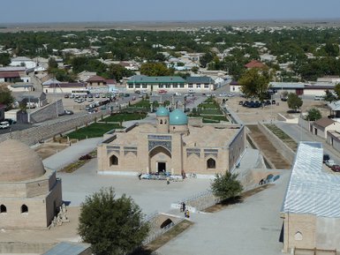 Eine weite Ansicht des Nurata Chashma-Komplexes, umgeben von grünen Bäumen und traditionellen Gebäuden in der Stadt.