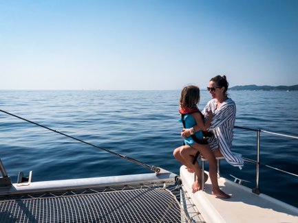 Eine Frau sitzt auf einem Boot und hält ein Kind, während sie den ruhigen Ozean und den blauen Himmel genießen.
