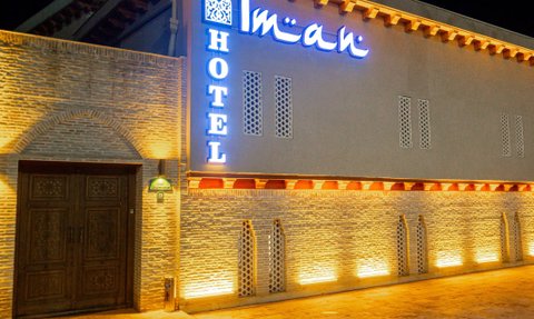 Die Fassade des Hotels Iman in Bukhara leuchtet nachts mit warmem Licht und einem auffälligen blauen Schild.