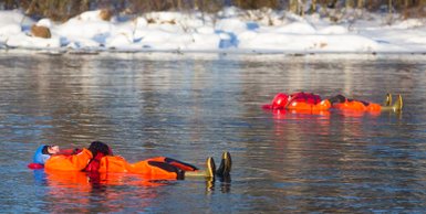 Zwei Personen in orangefarbenen Anzügen treiben entspannt auf einem ruhigen, schneebedeckten Fluss.