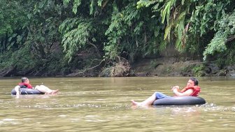 Zwei Personen treiben entspannt auf Reifen in einem ruhigen Fluss, umgeben von üppigem, grünem Dschungel.