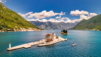 Eine malerische Küstenlandschaft mit einer kleinen Insel und einer Kirche, umgeben von Bergen und klarem Wasser.