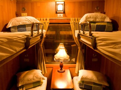 Ein gemütlicher Schlafwagen mit zwei Etagenbetten, einem Tisch und einer warmen Lampe, die eine einladende Atmosphäre schafft.