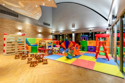 Ein bunter Spielbereich für Kinder mit verschiedenen Spielgeräten, darunter Rutschen, Tische und Spielzeugautos.