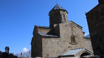 Eine alte Kirche mit einer markanten Kuppel steht vor einem strahlend blauen Himmel, umgeben von majestätischen Bergen.
