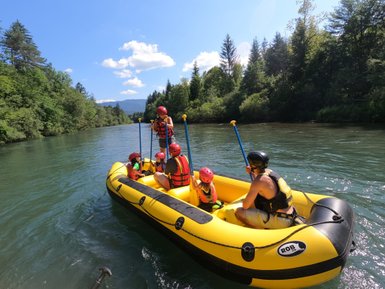Eine Gruppe von fünf Personen in einem gelben Schlauchboot paddelt auf einem ruhigen Fluss, umgeben von üppigem Grün.
