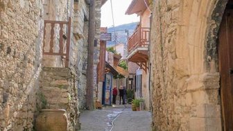 Eine enge Gasse mit steinernen Wänden, gesäumt von traditionellen Häusern und einem blühenden Topf auf dem Boden.