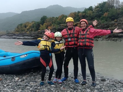 Eine fröhliche Familie posiert am Ufer eines Flusses, bereit für ein aufregendes Rafting-Abenteuer in der Natur.