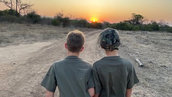 Zwei Kinder blicken auf einen farbenfrohen Sonnenuntergang in Makutsi – Südafrika Reise mit Kindern