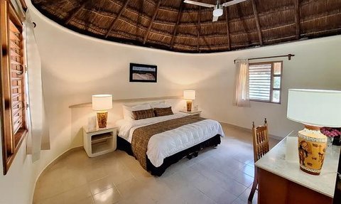 Ein gemütliches Hotelzimmer mit einem runden Strohdach, einem großen Bett und warmem Licht von den Nachttischlampen.