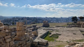 Die Ruinen eines antiken Tempels sind im Vordergrund sichtbar, während die Stadt Amman im Hintergrund liegt.