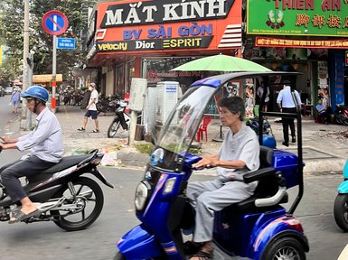 Eine belebte Straße in Saigon mit einem Mann auf einem blauen Elektroroller und verschiedenen Geschäften im Hintergrund.